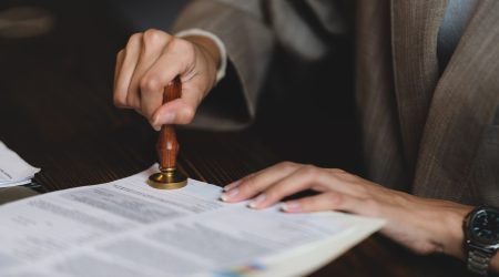 person's hand stamping with approved stamp on certificate document public paper at desk